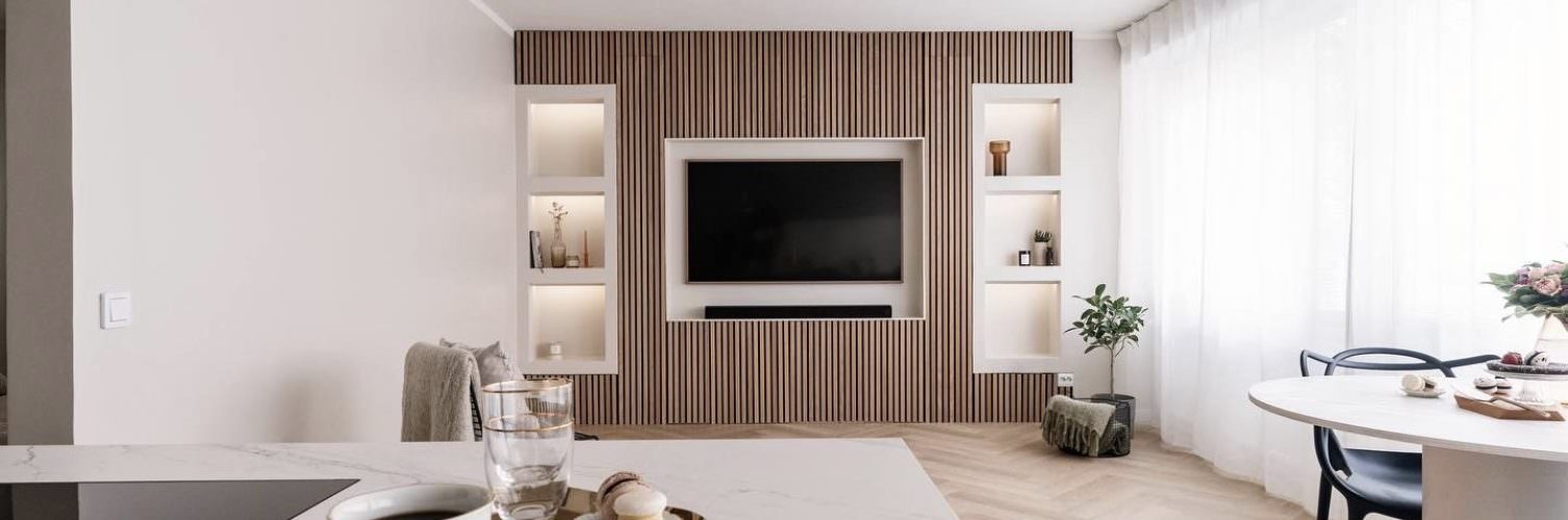 A stylish apartment with a white kitchen and wooden paneling, featuring slat wall panels in the kitchen area