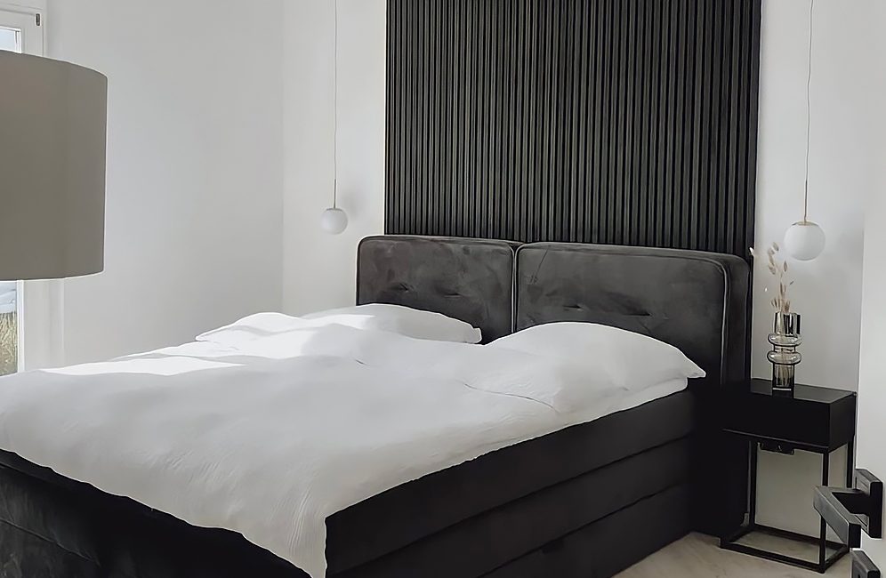 Contemporary bedroom design showcasing a black headboard, white bed, and elegant Acoustic Slat Panels in Black Ash for sound control.