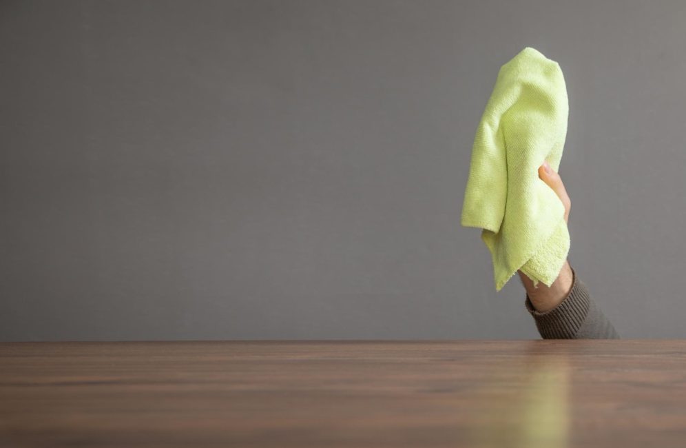 A person drapes a green cloth over a table, demonstrating a cleaning technique for wooden wall paneling.