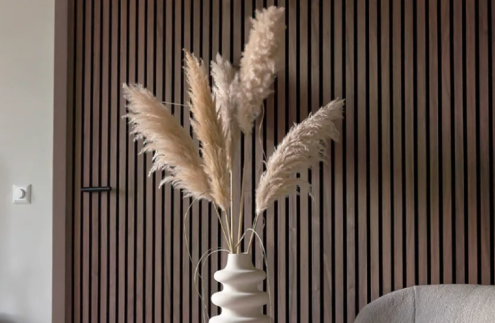 Tall pampas grass in a vase is displayed against a backdrop of rich walnut wooden paneling, enhancing the room's aesthetic.